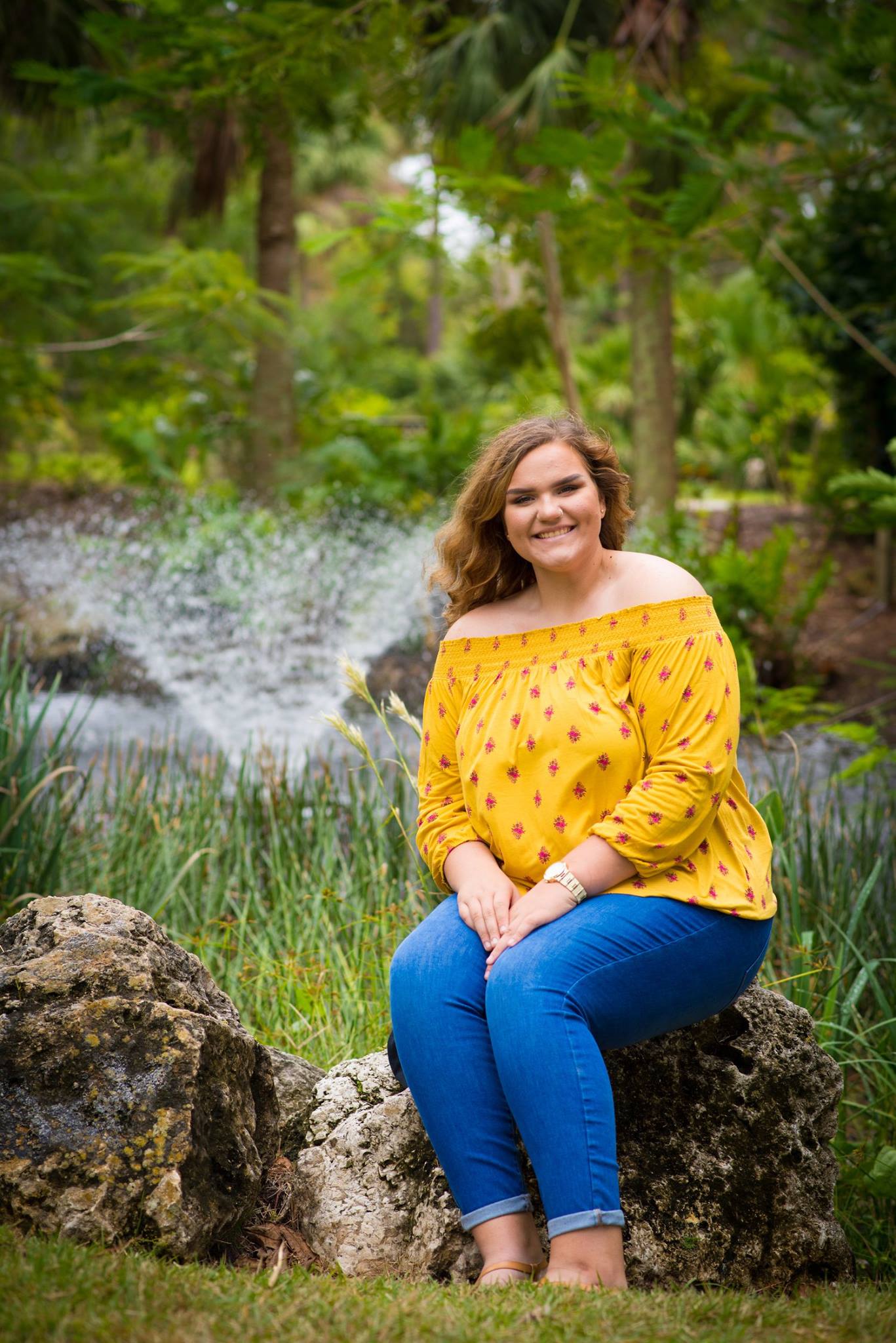 Senior sitting on mossy rocks with water fountain behind at Florida park