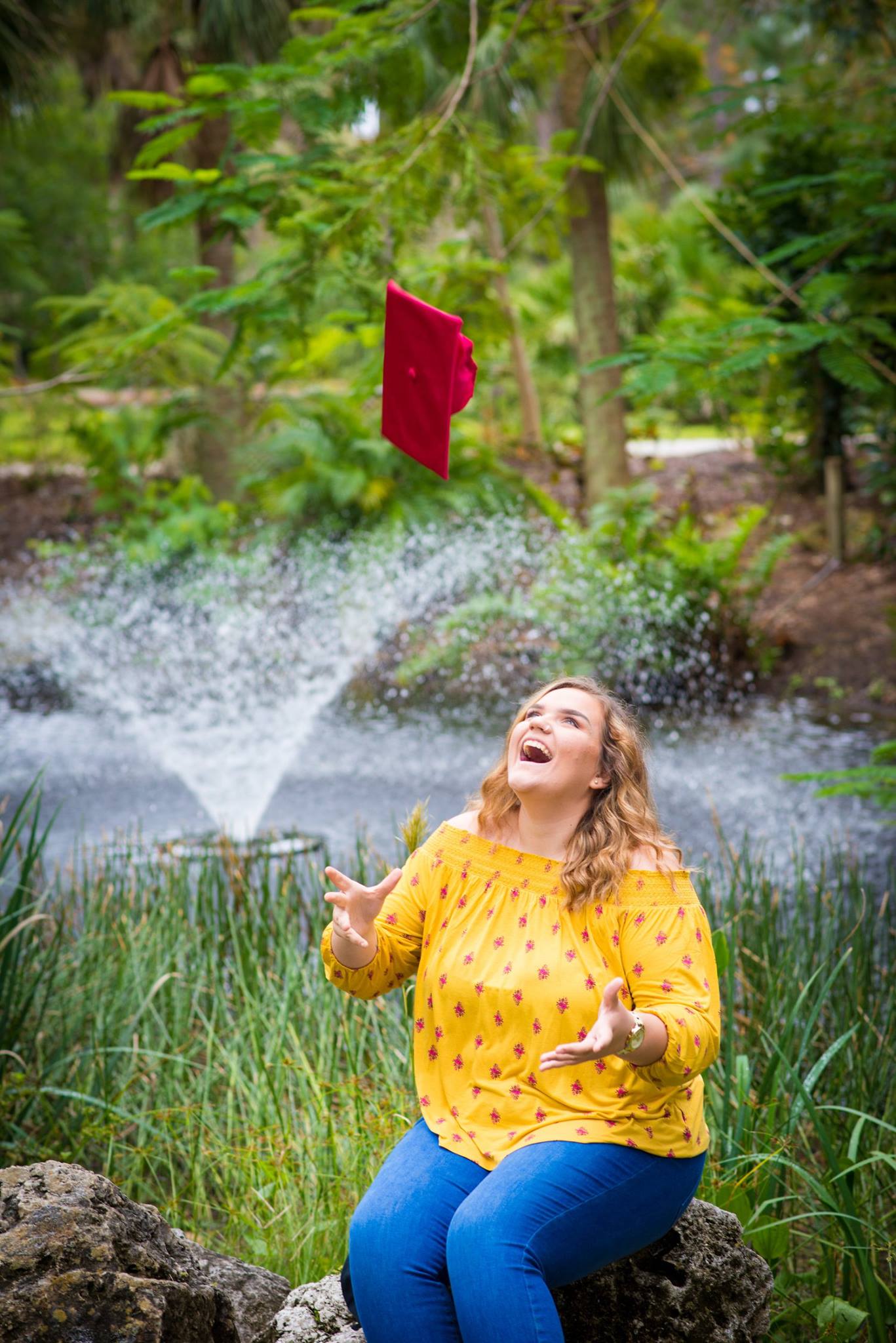 Senior tossing graduation cap at botanical garden fountain, Tampa Bay Florida